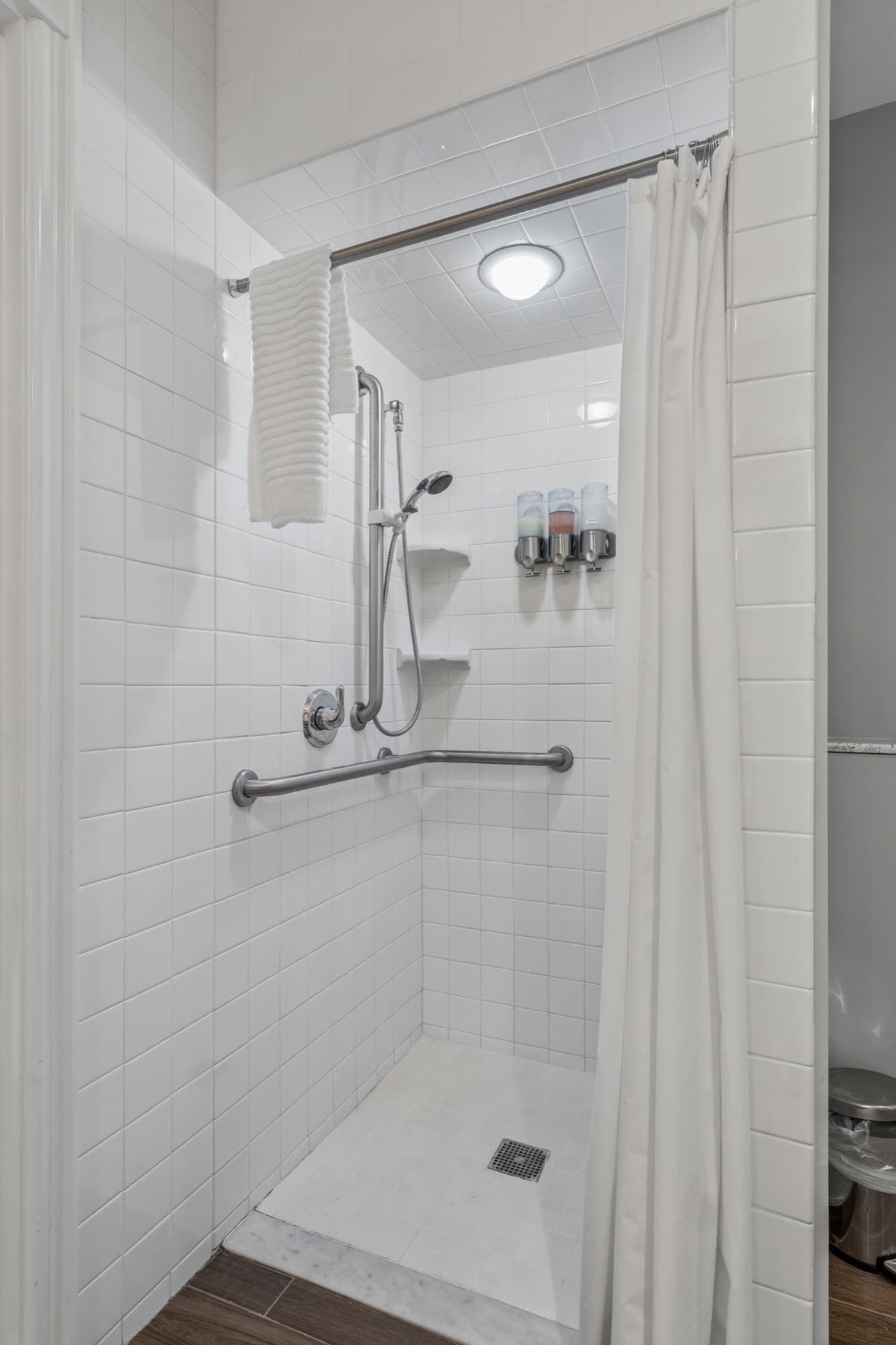 Accessible tile shower with grab bars, handheld shower head, and a curbless roll-in entry.