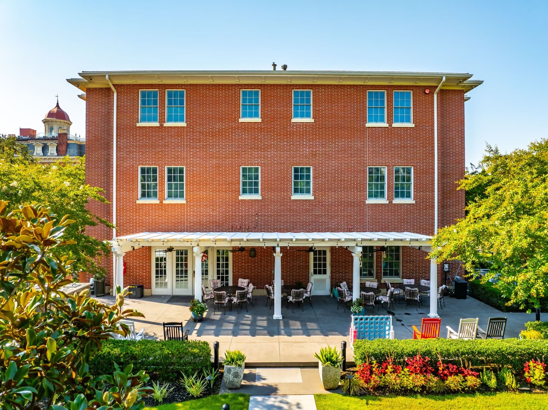 Rear exterior of the Charleston Fisher House showing a pergola-covered patio with fans, outdoor dining tables, rocking chairs, and lawn games.