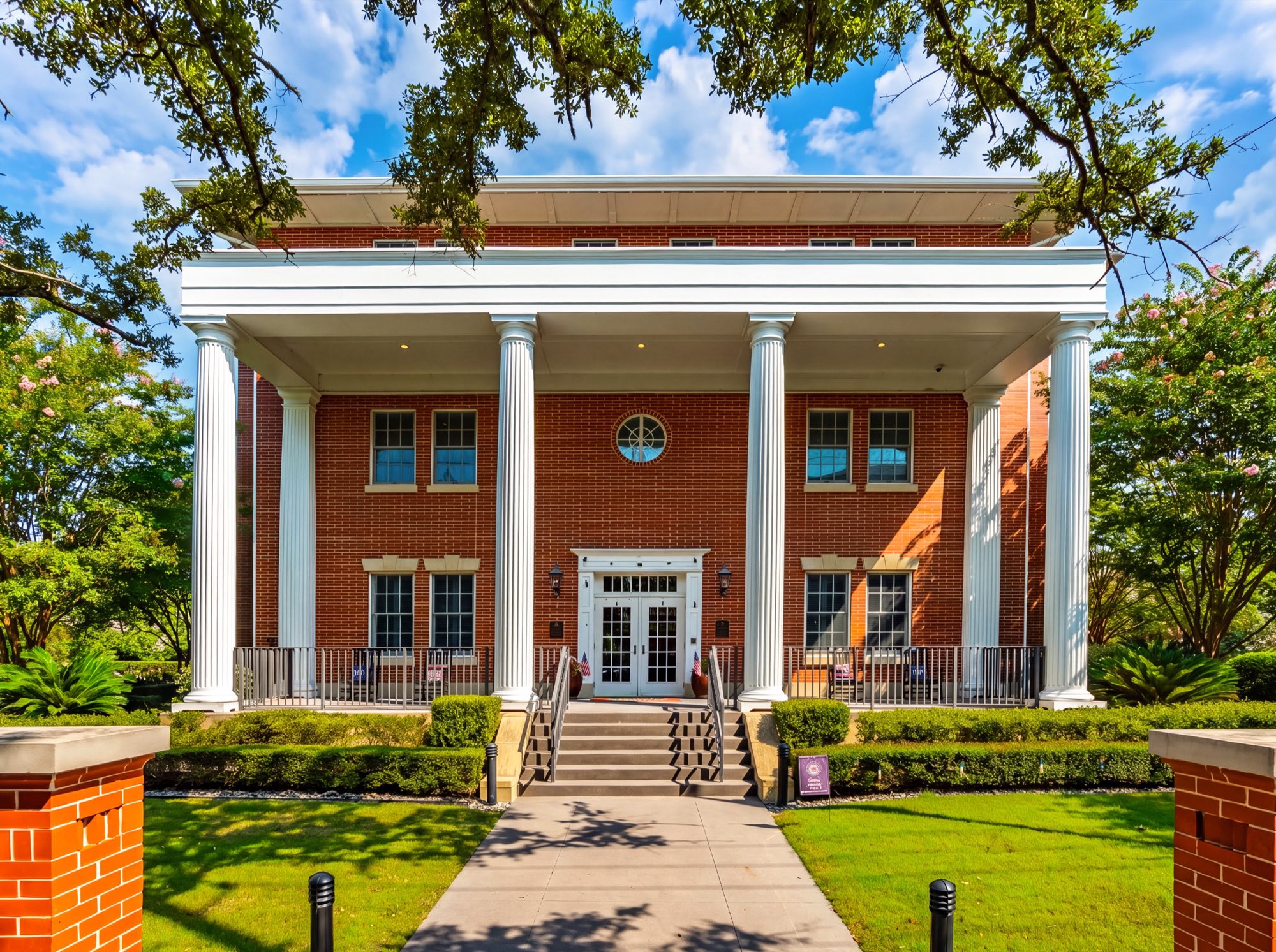 Straight-on view of the Charleston Fisher House, a brick home with a two-story white columned portico, under a blue sky
