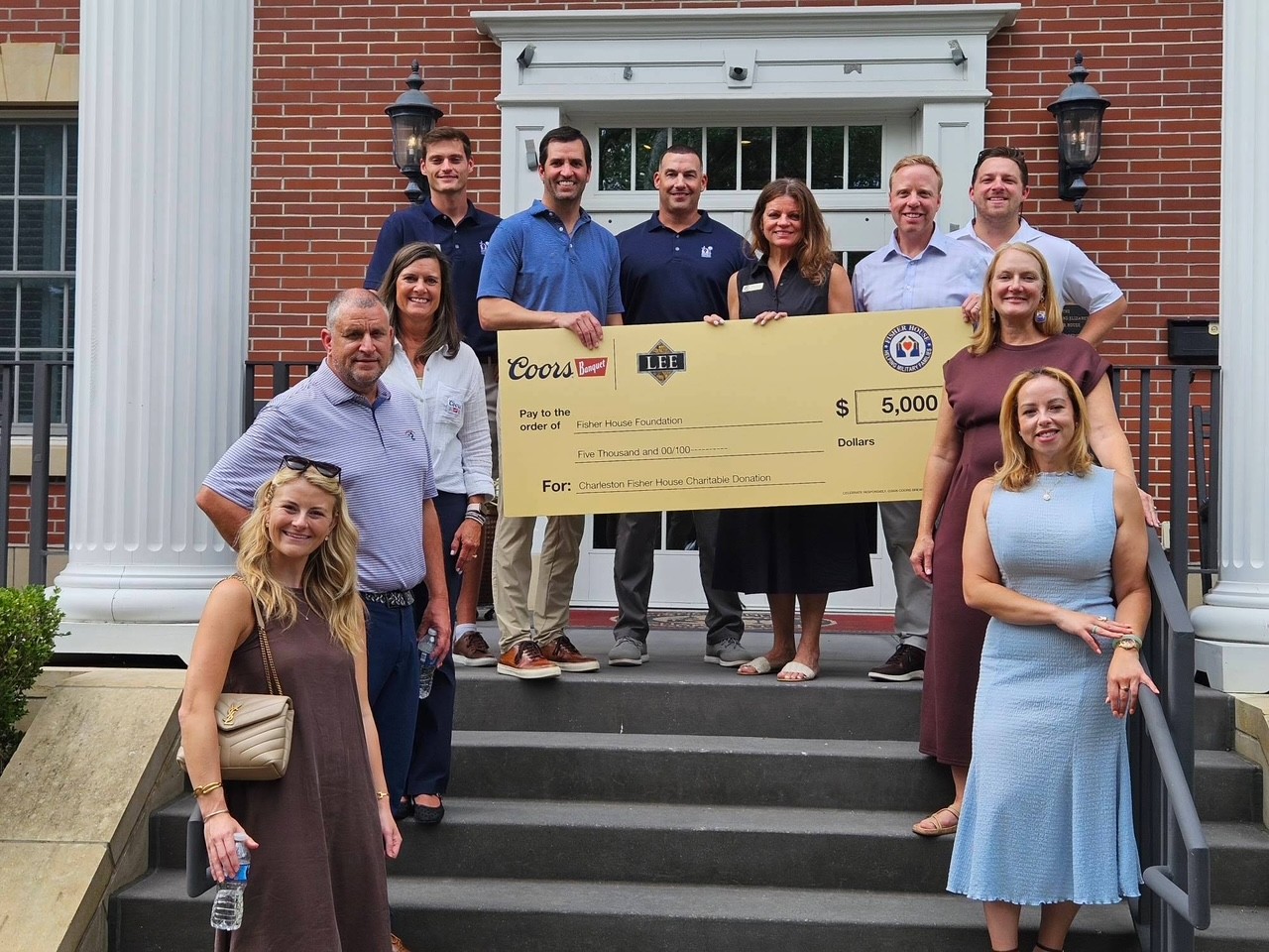 A group of Molson Coors and Lee Distributors representatives standing on the steps of the Charleston Fisher House holding a large $5,000 ceremonial check made out to the Fisher House Foundation
