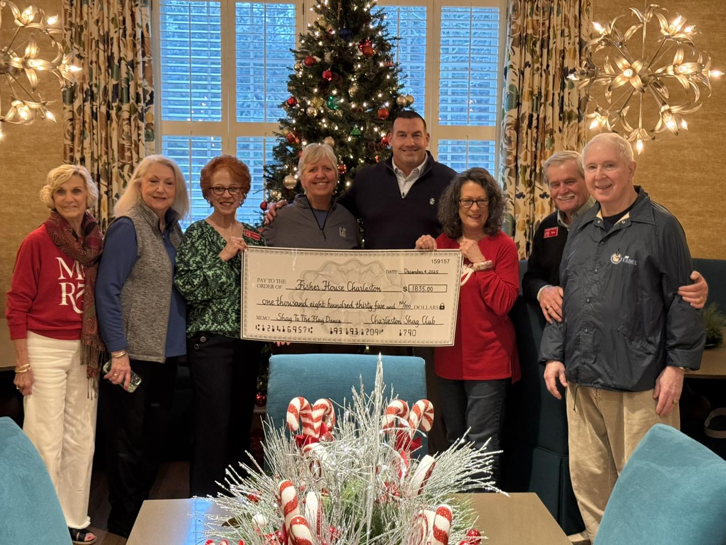 Charleston Shag Club members and Fisher House staff holding a $1,835 check inside the Fisher House living room decorated for Christmas